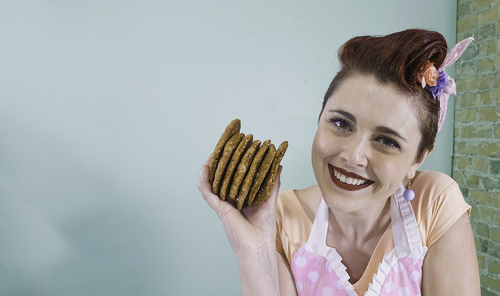 Katarina Poletto, owner of Dolled Up Desserts holding a stack of seven cookies while smiling