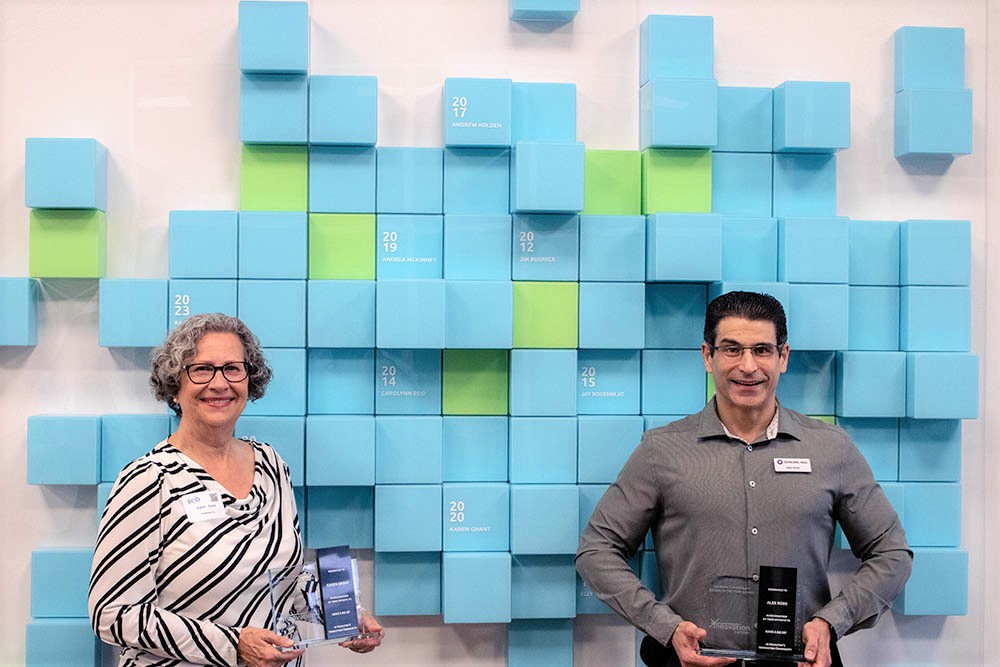 Mark Chamberlain DiFizen of the Year award winners Karen Grant and Alex Ross pose for photos with the Big DiFizen wall in McMaster Innovation Park