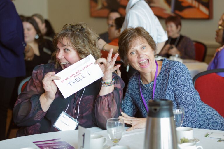 Two women at the 2023 HERhalton event happily displaying a sign before networking begins